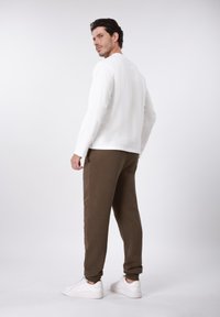 Λευκό πουκάμισο με μακριά μανίκια συνδυασμένο με καφέ φόρμα με ριμπ λεπτομέρειες στα πλάγια και λευκά αθλητικά, εμφανιζόμενο από πίσω γωνία.