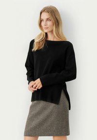 Mustmust mustril on paelise, pikkade varrukatega ja külgaukudega, koos halli herringbone seelikuga, millel on õrn textuur.