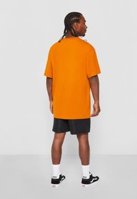 Tricou oversized portocalie, cu mâneci scurte, guler rotund și o textură fină din bumbac, asortat cu pantaloni scurți negri și adidași Vans.