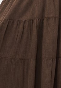 Καφέ ύφασμα με ρυτιδωτή, στρωματοποιημένη υφή που δημιουργεί απαλές οριζόντιες ραφές σε ελαφρύ, ελαφρώς τσαλακωμένο υλικό.