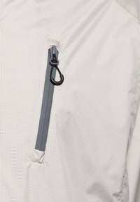 Jasnoszary materiał z delikatnym wzorem kratki, wyposażony w pionową wodoodporną kieszeń na zamek z czarną pętlą do ściągania.