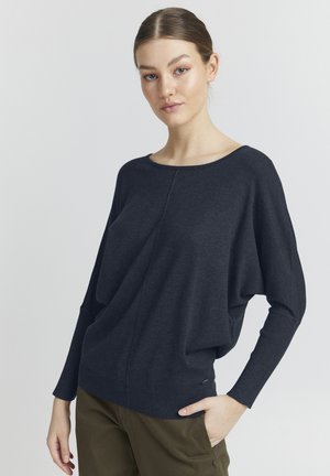 Pull long gris foncé à manches longues avec un large col, coupe décontractée, poignets côtelés et texture lisse. Porté sur un pantalon vert olive.