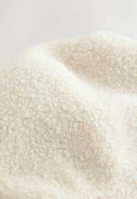 Cream-colored fleece fabric showcasing a soft, curly texture with a slightly shiny finish. The material appears plush and thick.