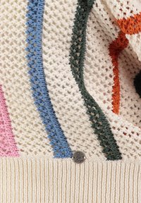 Primer plano de tela de punto con base color crema, con franjas verticales en rosa, azul, verde, naranja y una pequeña etiqueta metálica redonda.