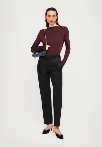 Woman wearing a long-sleeve maroon top, black high-waist trousers, black kitten heels, and holding a blue handbag over her shoulder.