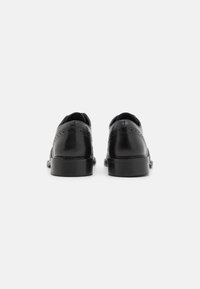 Scarpe in pelle nera con finitura liscia, punta arrotondata, tacco basso e dettagli decorativi a brogue lungo le cuciture.