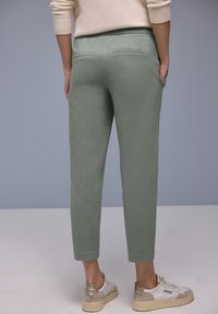 Zielone spodnie z mieszanki bawełny o zwężanym kroju, z dwoma tylnymi kieszeniami i kontrastującym przeszyciem, zestawione z białymi i beżowymi sneakersami.