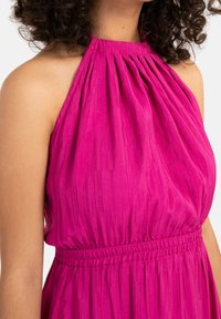 Magenta halterneckklänning med veckad textur, elastisk midja och en flödande silhuett. Slät tyg med subtil glans.