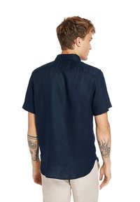 Maglietta blu navy a maniche corte realizzata in tessuto leggero, con colletto button-down e orlo dritto. Tessuto liscio senza motivi.