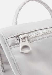 Hvid stofpose med en tekstureret overflade, der har en hvid lynlås og et vævet håndtag, som fremhæver lynzsens detaljer og syninger.