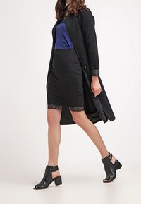 Czarna spódnica z koronkową lamówką, niebieska bluzka oraz czarny długi płaszcz. Obuwie to czarne sandały na obcasie typu słupek z paskami, odsłaniające palce.