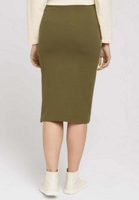 Jupe mi-longue vert olive en matière texturée, coupe ajustée avec un ourlet arrivant sous le genou. Assortie à des chaussures blanches montantes décontractées.