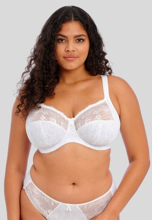 Witte kanten bh met semi-transparante cups, een stippenpatroon en verstelbare bandjes. Bevat een klein strikje in het midden en kanten accenten.