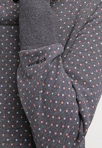 Sudadera gris con pequeños lunares rosas y morados. Presenta una tela texturizada y un logo bordado en el puño.