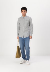 Striped button-up shirt in white and navy, blue jeans, and white sneakers. Holding an olive green tote bag. Simple, casual outfit.