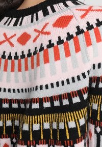 Sweter dzianinowy z wielokolorowymi geometrycznymi wzorami w kolorze czarnym, różowym, czerwonym, szarym i żółtym. Rybkowany czarny dekolt oraz różnorodne faktury.