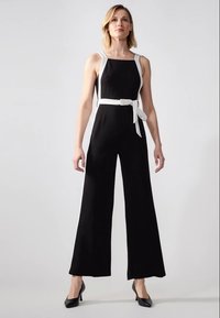 Mono negro de pierna ancha, con tirantes blancos y un cinturón a juego en la cintura. Tejido suave, diseño minimalista y ajuste entallado.