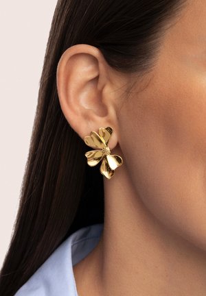 Gouden bloemenoorbellen met een gevarieerd ontwerp, met bloembladvormen en een centrale kraal, gedragen aan een oor tegen een gladde huid.