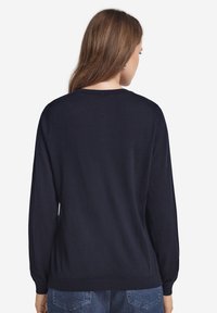 Marinblå långärmad tröja i mjukt material med en enkel design på baksidan, ribbade ärmslut och nederkant. Inga synliga dekorationer.