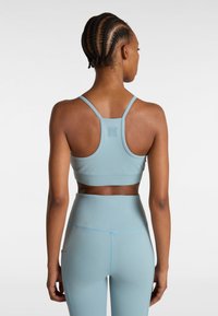 Lichtblauw sportbh met dunne straps, zachte textuur en een logo aan de achterkant. Gecombineerd met hoge taille sportleggingen die zakken hebben.