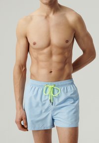 Jasnoniebieskie szorty kąpielowe z elastycznym paskiem w talii oraz neonowożółtym sznurkiem z metalowymi końcówkami. Gładka tekstura materiału, długość do połowy uda.