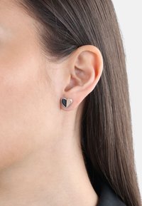 Pendientes en forma de corazón que presentan un segmento negro y uno beige, montados en metal de tono plateado con un acabado pulido.