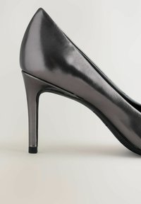 Fémes szürke magassarkú cipő, hegyes orral és sima felületstruktúrával, karcsú sarokkal. Fekete talppal rendelkezik, és nincsenek látható díszítések.