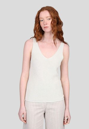 Débardeur blanc à côtes avec un décolleté en V profond. Le tissu a une finition texturée. Associé à un pantalon large à rayures claires.
