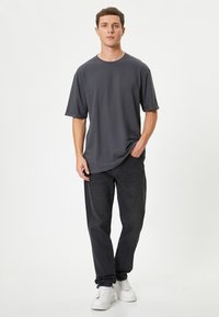 Mørkegrå kortærmet t-shirt med en afslappet pasform, stylet med mørke jeans og hvide sneakers. Glat stof, rund halsudskæring og afslappet stil.