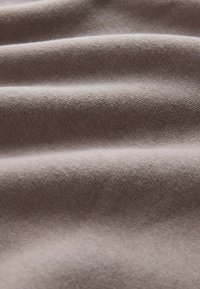 Šedá strukturovaná tkanina s viditelnými vlnkovými vzory. Měkký materiál vytváří jemnou hloubku a stínování po celé ploše.