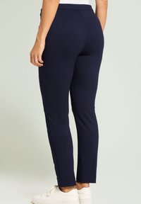 Pantalones ajustados en azul marino con una textura suave, que cuentan con una cintura alta y aberturas laterales en el dobladillo, combinados con zapatillas blancas.