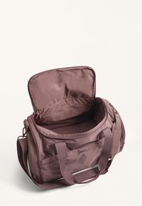 Purple fabric duffle bag with two top handles and a shoulder strap. Open zipper shows spacious interior with a zippered pocket. Smooth texture.