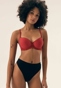 Czerwony stanik z koronkowym wykończeniem i gładką powierzchnią, z regulowanymi ramiączkami, w połączeniu z czarnymi, prążkowanymi majtkami o wysokim stanie.
