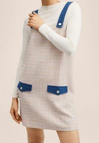 Robe tissée avec un tissu texturé aux couleurs pastel, dotée de bretelles bleues et de poches avec fermetures à pression. Forme simple en A.