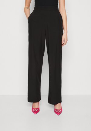 Pantalons larges noirs à taille haute avec poches avant, associés à des escarpins roses vifs à bout pointu ornés d'accents en forme de cœur.