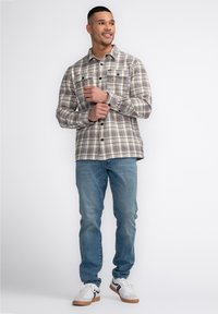 Grau-beige kariertes Flanellshirt mit zwei Brusttaschen, knöpfbaren Bündchen, getragen mit hellblauen Jeans und weißen Sneakers.