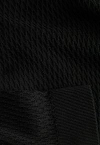 Gros plan sur un tissu tricoté noir montrant des textures côtelées et torsadées avec un détail de bord plié.