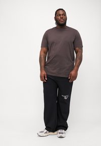 Brown short-sleeve t-shirt paired with black sweatpants featuring white logo embroidery, worn with gray and white sneakers.