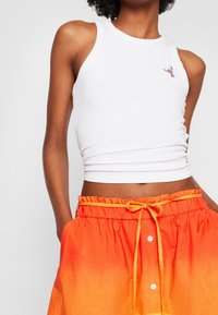 Weißes, geripptes Tanktop mit rundem Ausschnitt, kombiniert mit einem orangefarbenen Ombre-Rock mit Kordelzug und Knöpfen an der Vorderseite.
