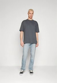 Tamnosiva oversized majica kratkih rukava i okruglog ovratnika. Nošena s svijetloplavim trapericama i crno-bijelim tenisicama.