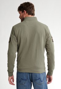 Olivgrüner Sweatshirt mit hohem Kragen, gerippten Bündchen und Saum; mit Patches an beiden Ärmeln; weiche Textur, lockere Passform.