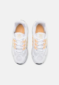 White athletic shoes with mesh upper, featuring orange accents and three side stripes. Laced design, textured sole, and padded collar.