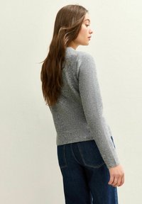 Pull en tricot gris au design ajusté, col rond et manches longues. La texture semble douce et il est associé à un denim bleu foncé.