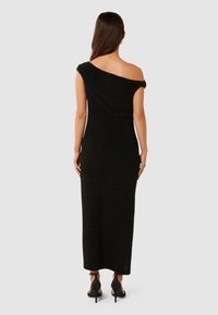 Rochie maxi neagră, cu umerii la vedere, dintr-un material texturat, cu siluetă ajustată și detalii cu nervuri; purtată cu pantofi cu toc înalt negri.