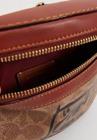 Brun läderpås med en texturerad yta, som har en gulddragkedja, vinröd foder och en liten varumärkesetikett inuti.