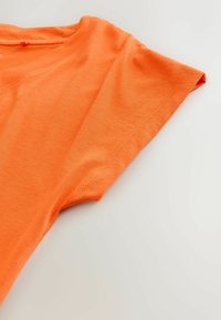 Kurzärmliges oranges Baumwoll-T-Shirt mit rundem Ausschnitt, sichtbaren Nähten entlang der Schultern und Ärmelränder vor hellem Hintergrund.