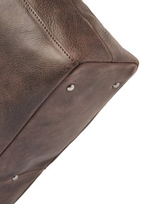 Bruine leren tas met een gestructureerde afwerking, vierkante vorm, zichtbare stiksels en metalen studs aan de onderkant ter versterking.