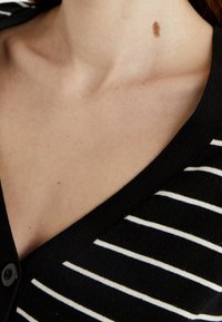 Zwarte cardigan met horizontale witte strepen, knoopdetail en V-halsontwerp; materiaal lijkt zacht met een gladde textuur.