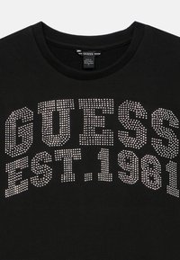 Μαύρο φούτερ με την επιγραφή "GUESS EST. 1981" σε ασημί στρας. Στρογγυλή λαιμόκοψη και ριμπ τελείωμα. Μαλακό ύφασμα με απαλή υφή.