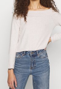 Pull rose pâle à épaules dénudées avec manches longues, associé à un jean en denim bleu taille haute présentant un design classique à cinq poches.